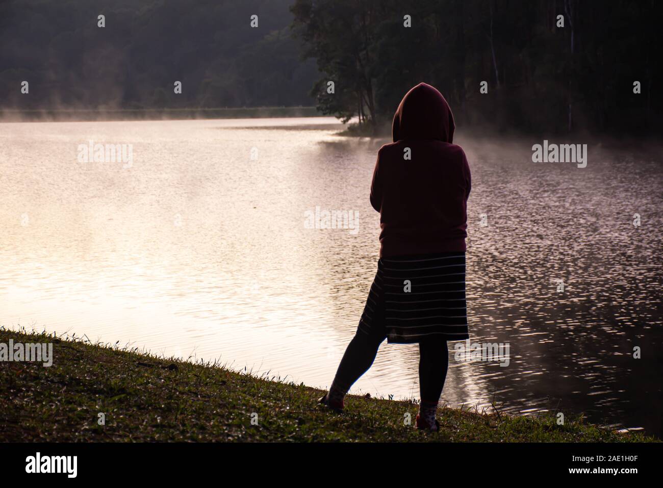 The image behind Woman standing on the lawn And mist floating over the water at Pang Tong reservoir in Mae Hong Son , Thailand. Stock Photo