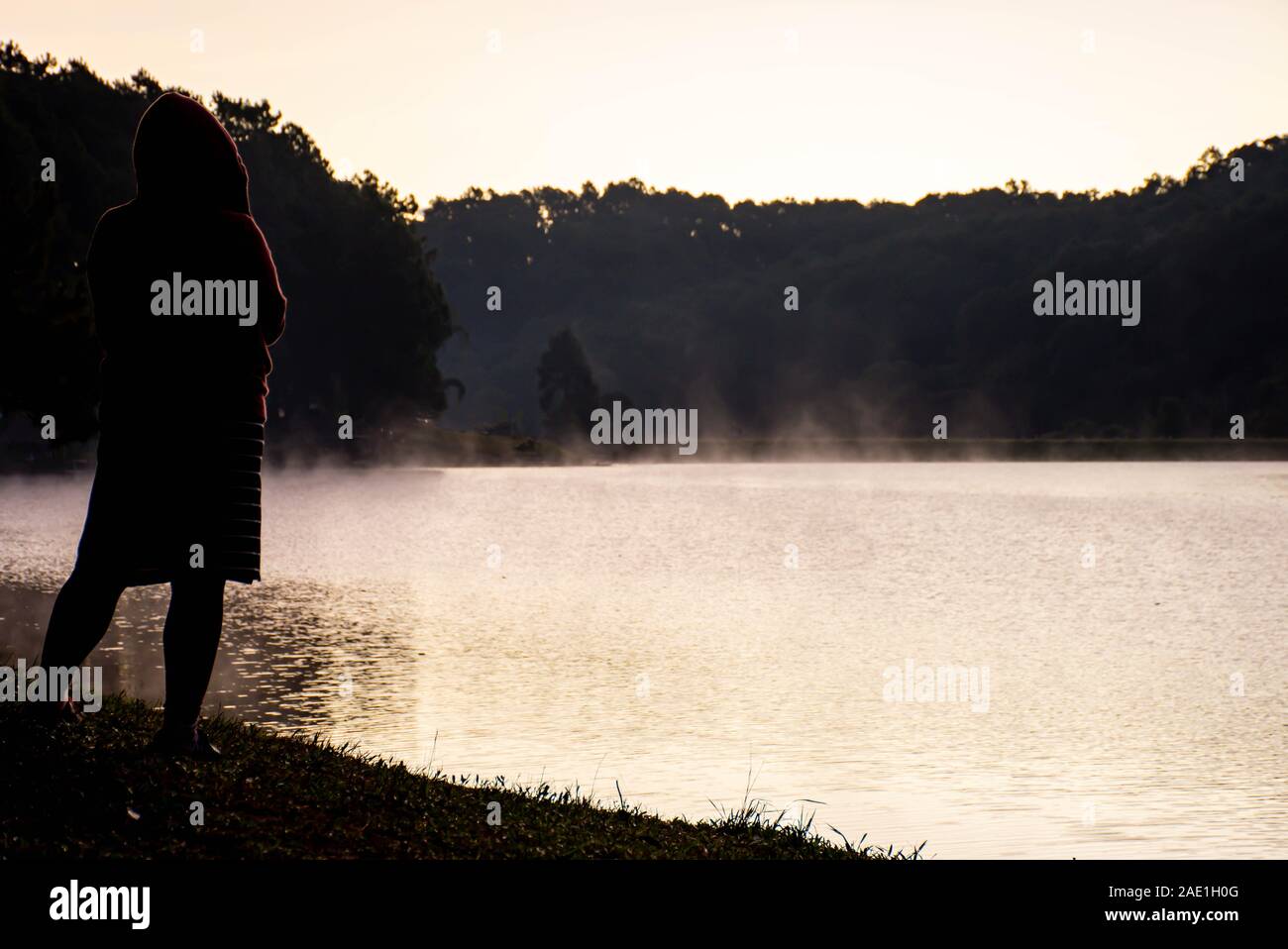 The image behind Woman standing on the lawn And mist floating over the water at Pang Tong reservoir in Mae Hong Son , Thailand. Stock Photo