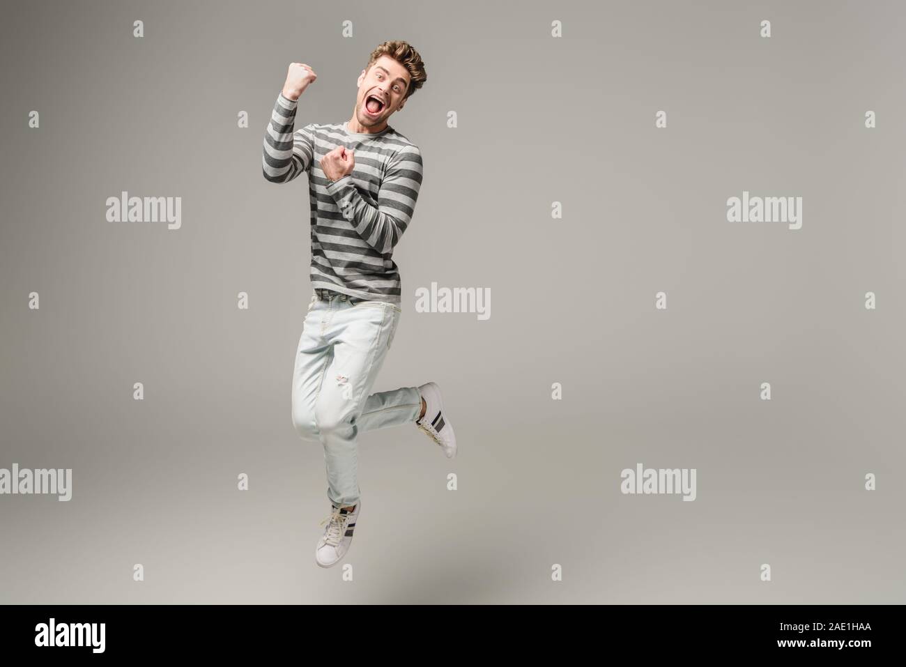 excited screaming man jumping and cheering on grey Stock Photo
