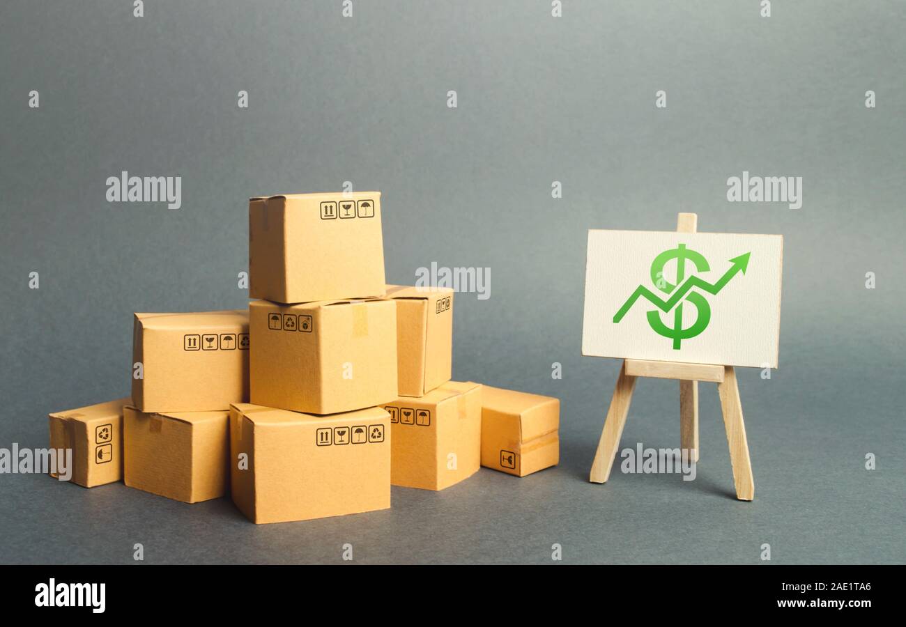 A pile of cardboard boxes and a stand with green arrow up. Increasing consumer demand. rate growth of production of goods, increasing economic indicat Stock Photo