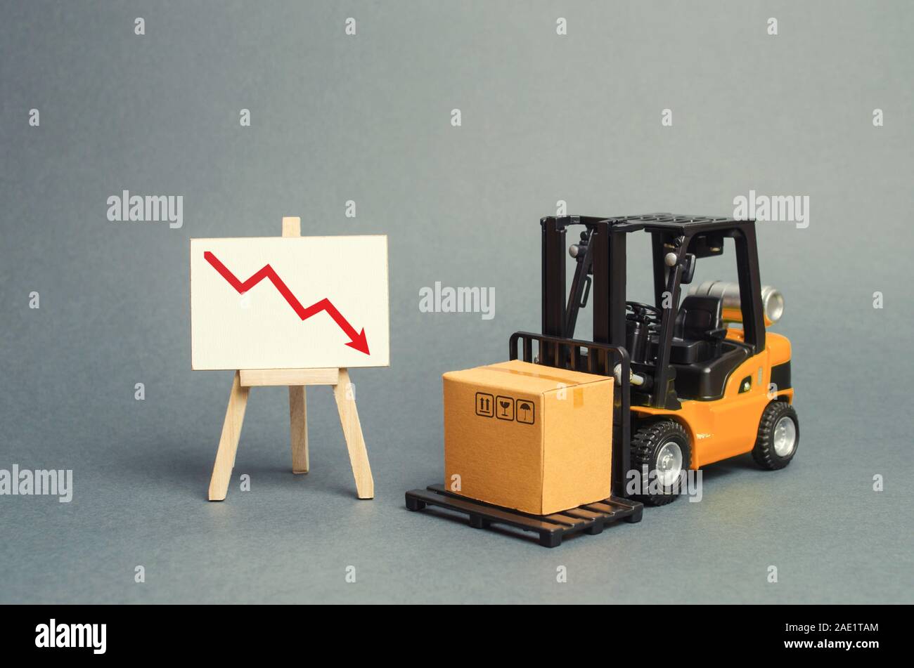 Forklift truck carries a cardboard box near a stand with a red arrow down. decline in the production of goods and products, economic downturn and rece Stock Photo