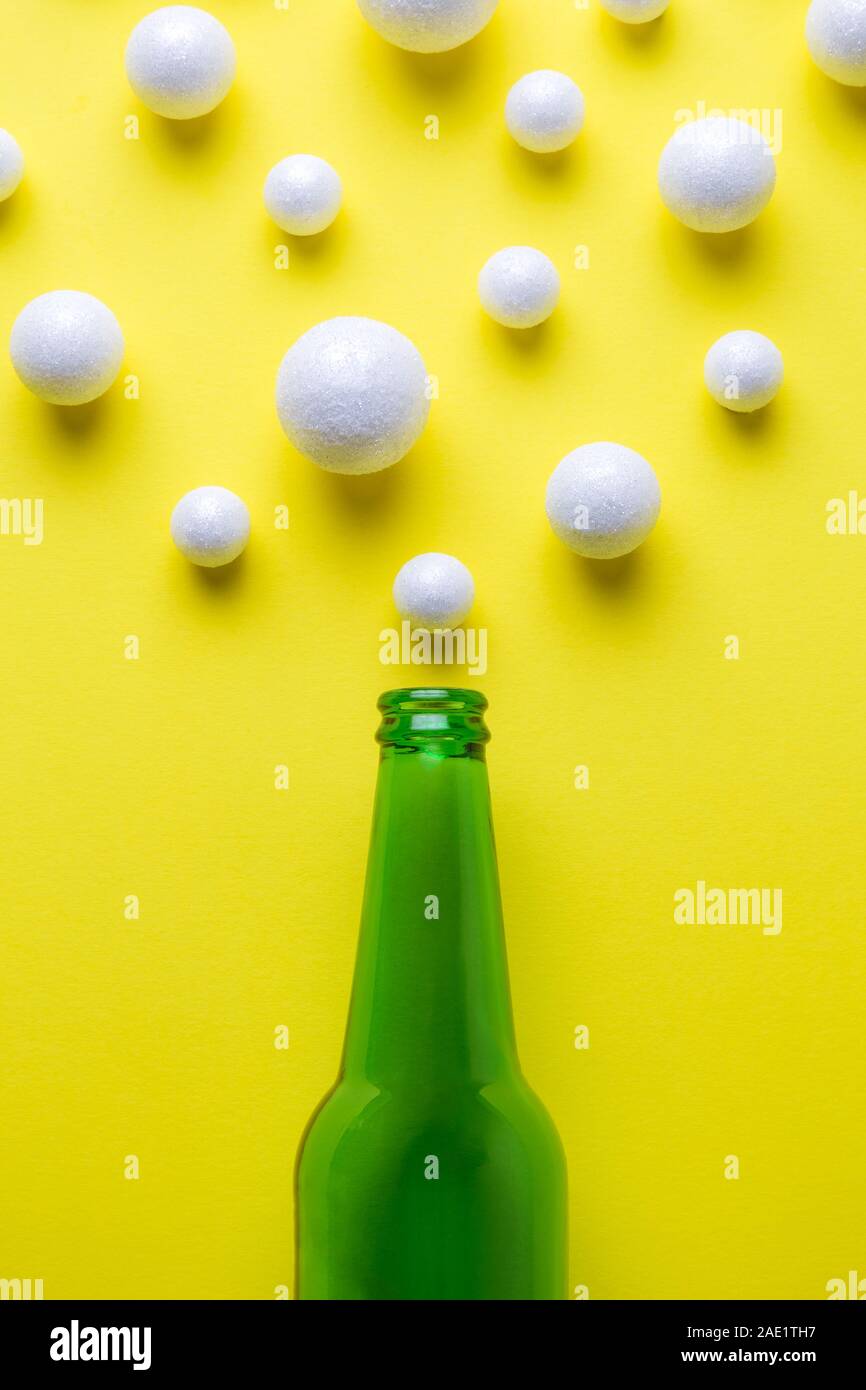 Flat lay of green beer bottle and bubbles made of styrofoam balls against yellow background minimal creative drink concept. Stock Photo