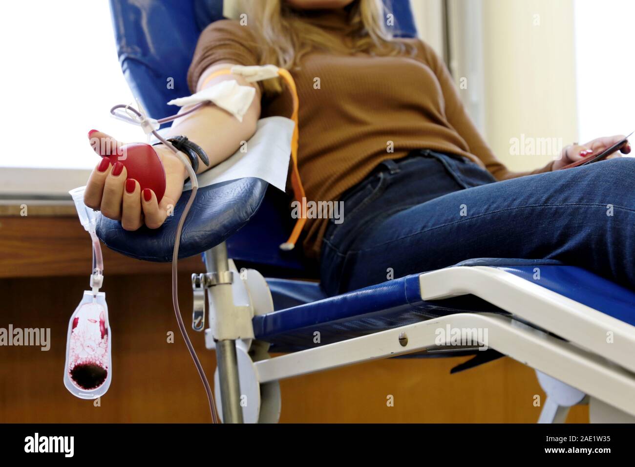 Blood donation, girl donor in chair with a red bouncy heart in hand. Concept of donorship, transfusion, health care Stock Photo