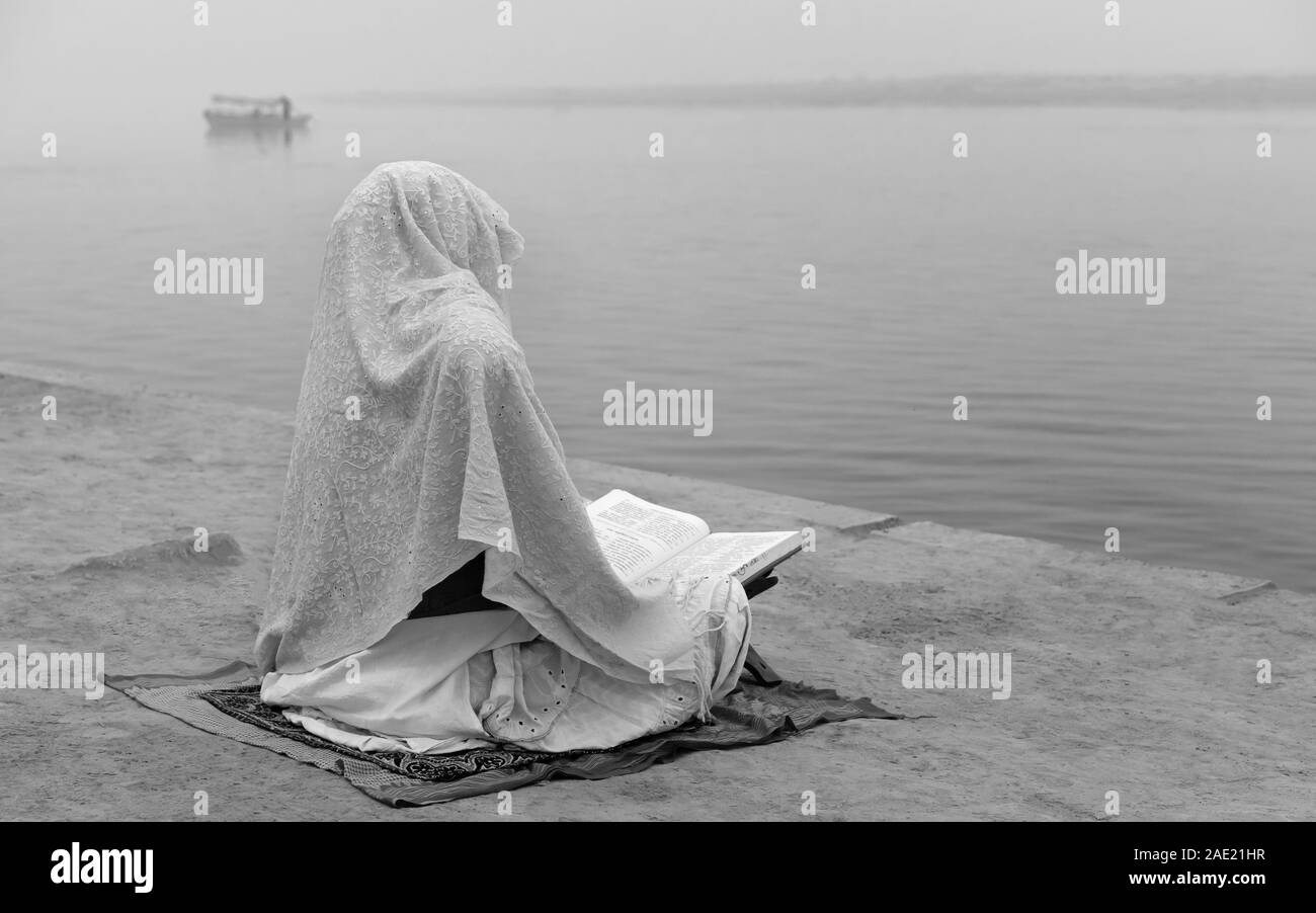 Solitary Hindu woman covered in shawl deep in mediation on bank of river Yamuna at dawn in Vrindavan, Uttar Pradesh, India. Stock Photo