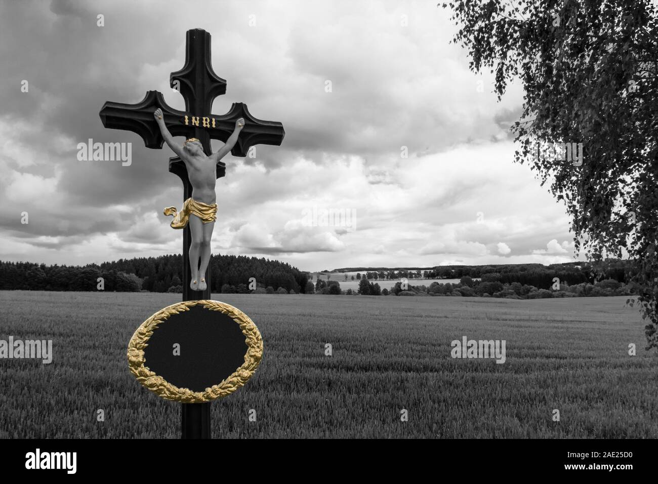 Jesus Christ crucifix in black-white rural landscape. Cornfield and dramatic sky. Vintage metal religious cross closeup. Copy space in oval gold frame. Stock Photo