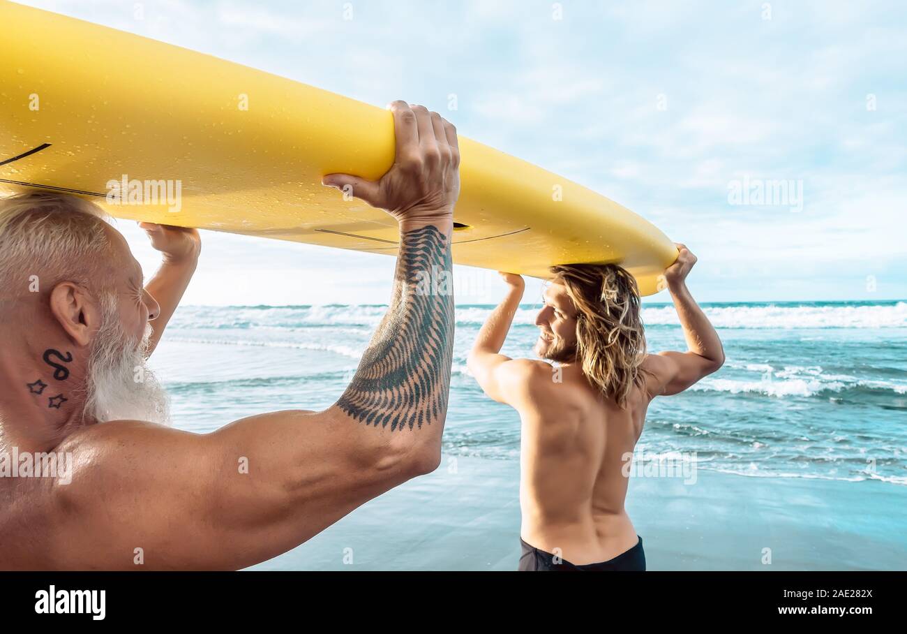 Happy fit friends having fun surfing on tropical ocean - Surfers father and son doing stretching surf exercises Stock Photo