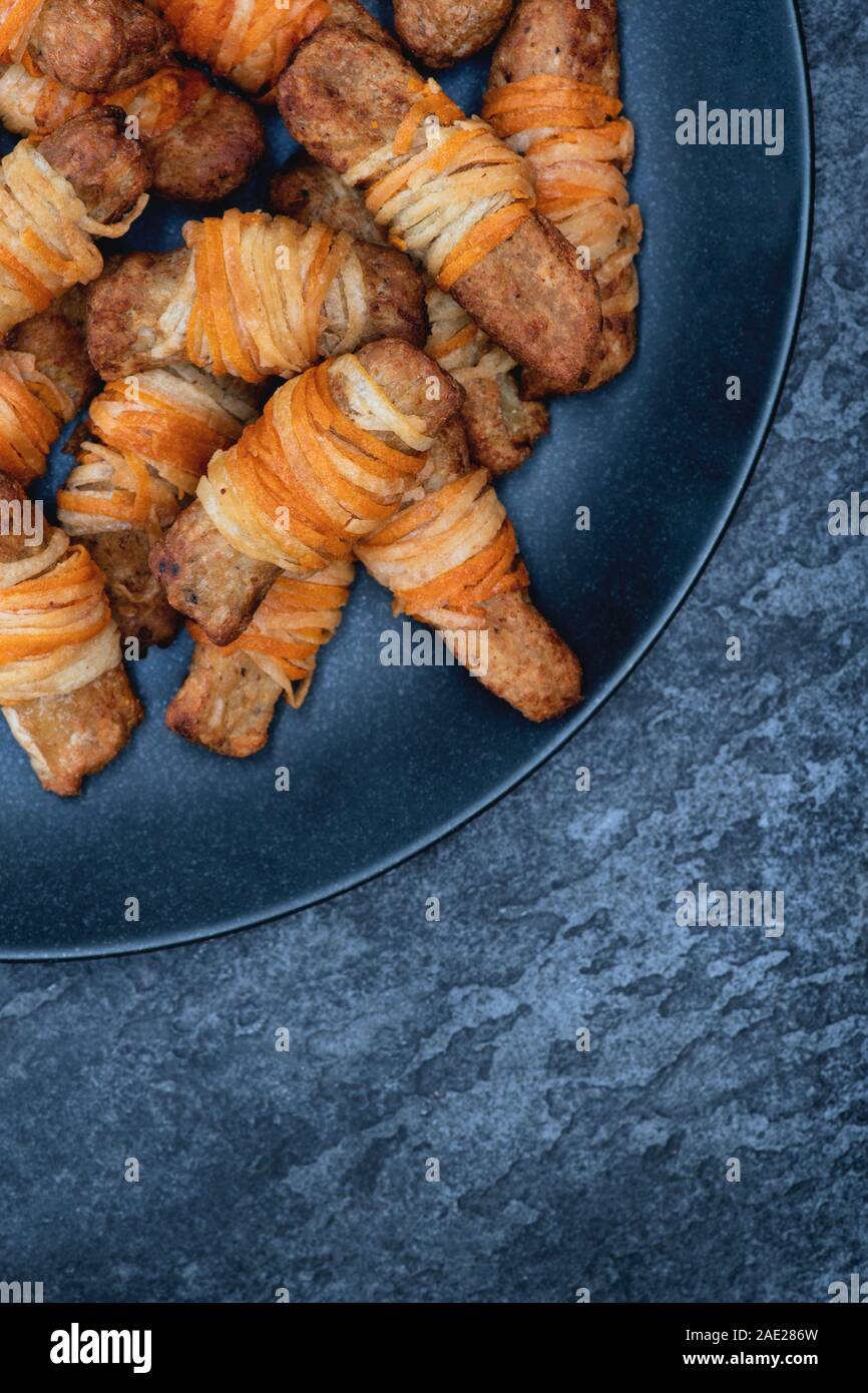 Vegan pigs in blankets in a tray on a slate background. Cooked