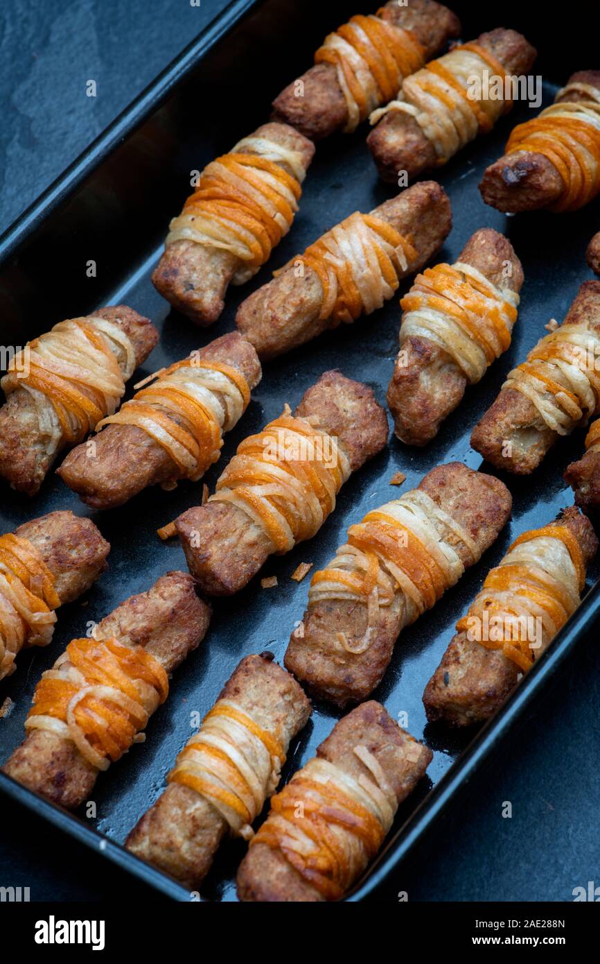 Vegan pigs in blankets in a tray on a slate background. Cooked