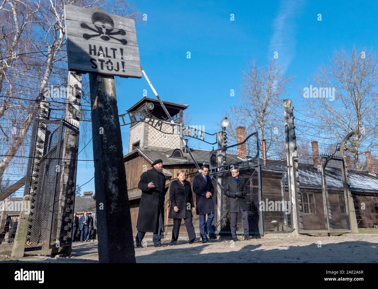 dpatop - 06 December 2019, Poland, Oswiecim: Federal Chancellor Angela Merkel (CDU) visits the former German Auschwitz concentration camp and walks under the entrance gate with the words 'Arbeit macht frei' (Work makes free) together with Polish Prime Minister Mateusz Morawiecki (to the right of Merkel) and Piotr Cywinski (to the left of Merkel), Director of the Auschwitz-Birkenau Memorial and President of the Auschwitz-Birkenau Foundation. Andrzej Kacorzyk, Deputy Director of the Auschwitz-Birkenau Museum, goes to the far right. Merkel accepted an invitation from the Auschwitz-Birkenau Founda Stock Photo