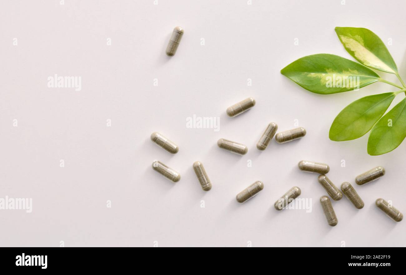 Background with capsules of natural medicine and plant on white table. Natural medicine concept. Top view. Horizontal composition. Stock Photo