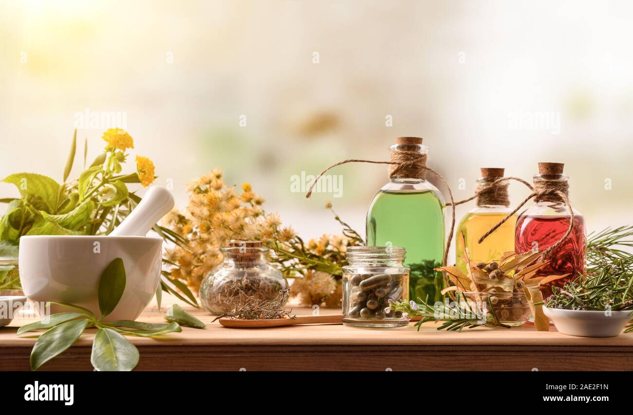 Composition of natural alternative medicine with capsules, essence and plants on wooden table in rustic kitchen. Front view. Horizontal composition. Stock Photo