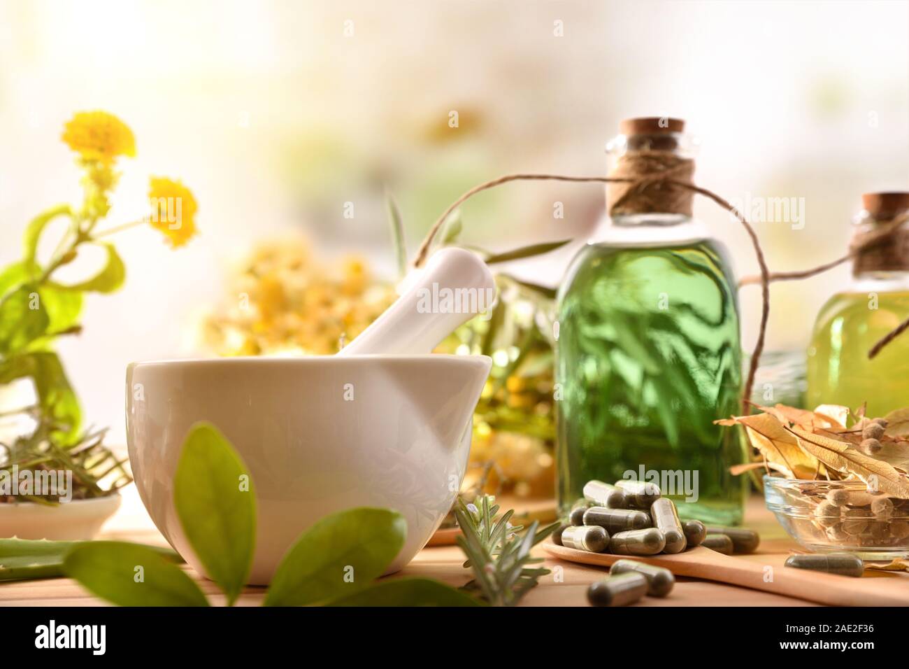 Capsules and bottles of essence of natural medicine with medicinal plants on wooden table in rustic kitchen. Front view. Horizontal composition. Stock Photo