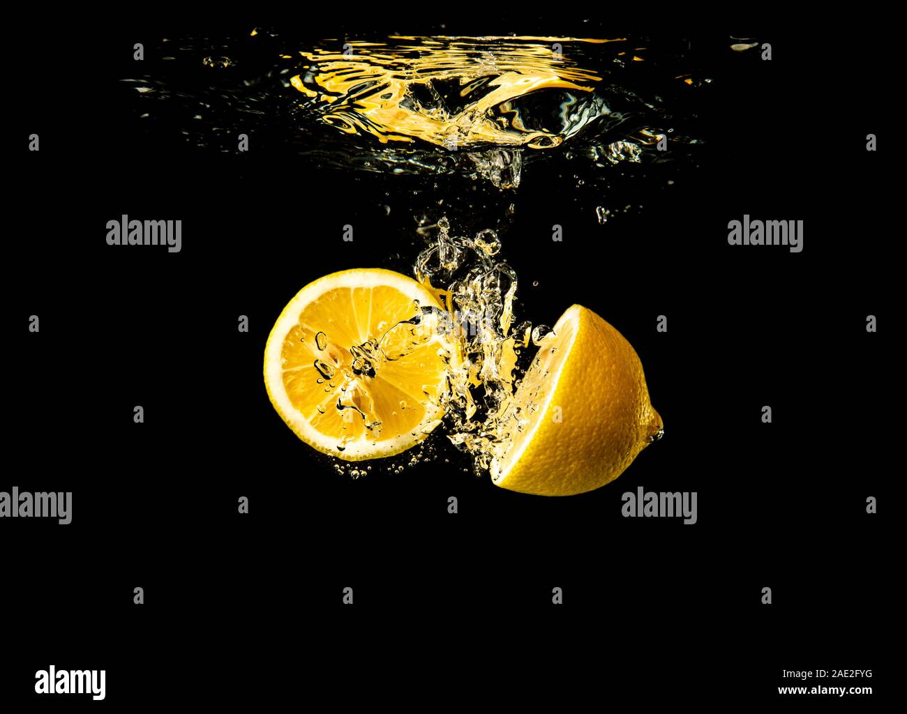 Fresh yellow lemon halves in water splash on black background with lots of air bubbles. Stock Photo