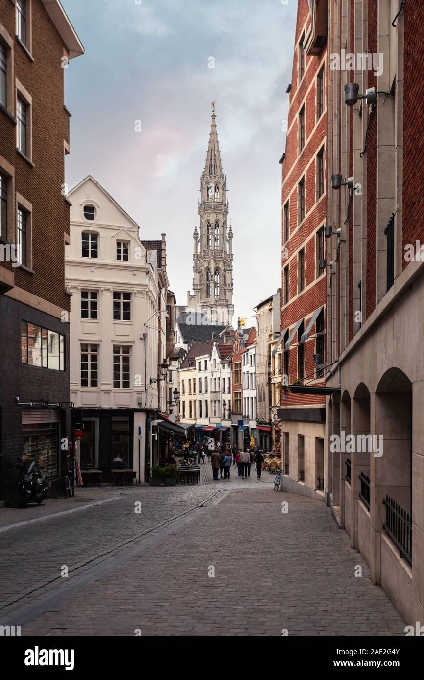 A small street in the historical part of Brussels with many restaurants and the Brussels Town Hall tower in the background, Belgium Stock Photo