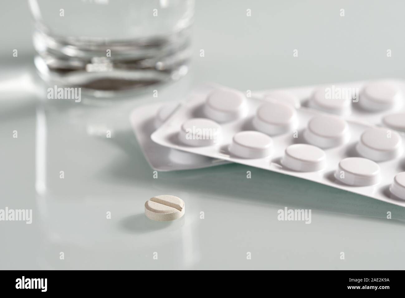 White still life with an antibiotic pill lying on a glass plate in front of two blister packs with tablets and a glass of water Stock Photo