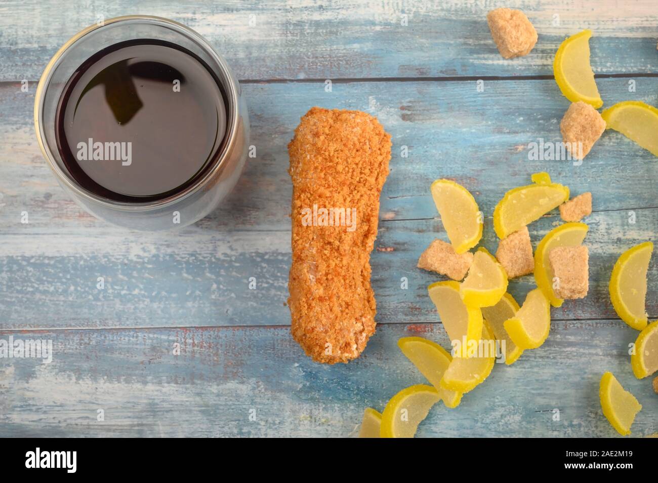 A glass of black tea, one cake and marmalade lemon slices on a wooden background Stock Photo