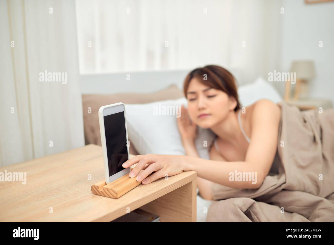 Annoying alarm. Woman lying in bed being woken by mobile phone, turning