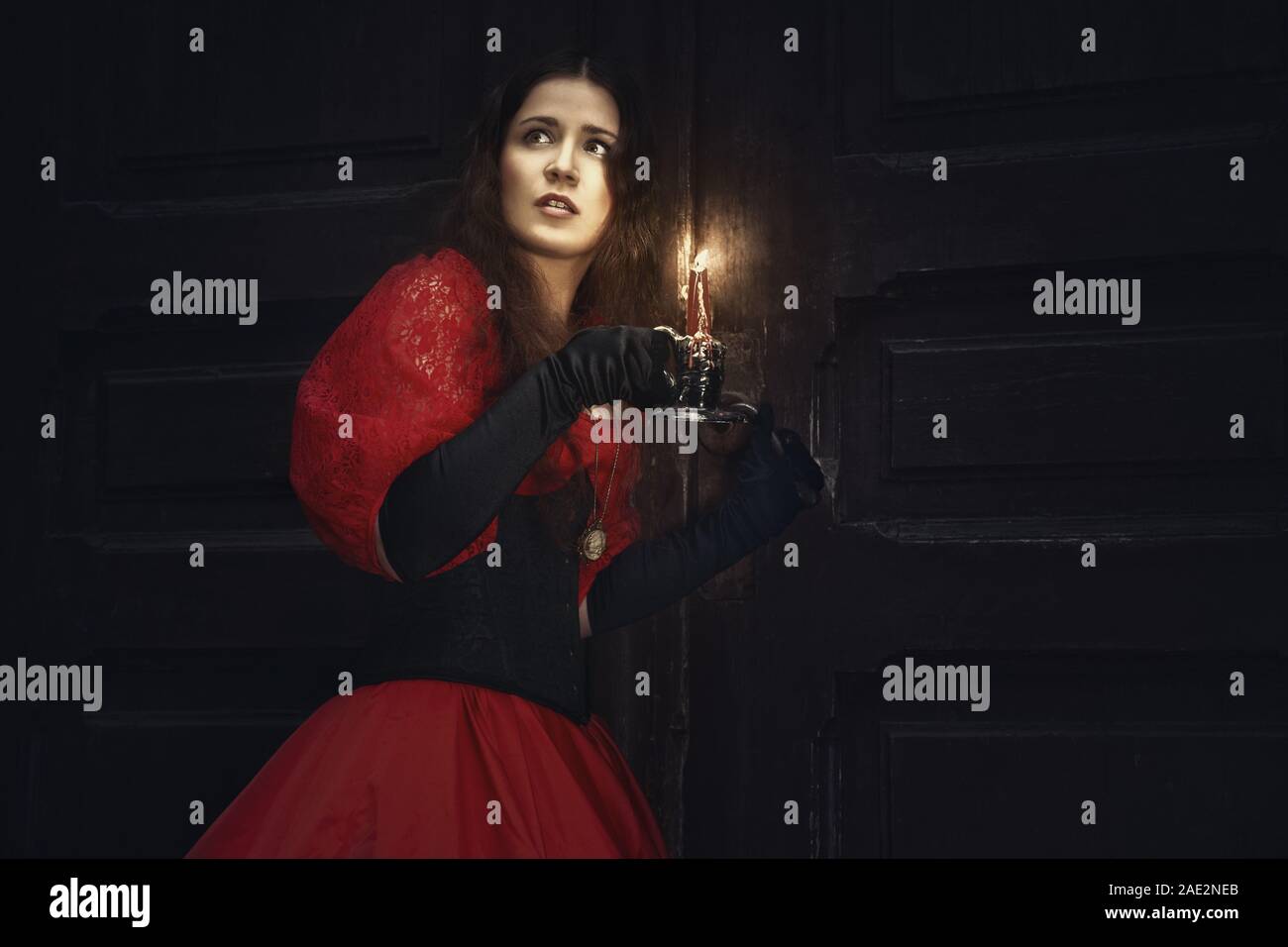Mysterious woman in a red Victorian dress by the old door Stock Photo