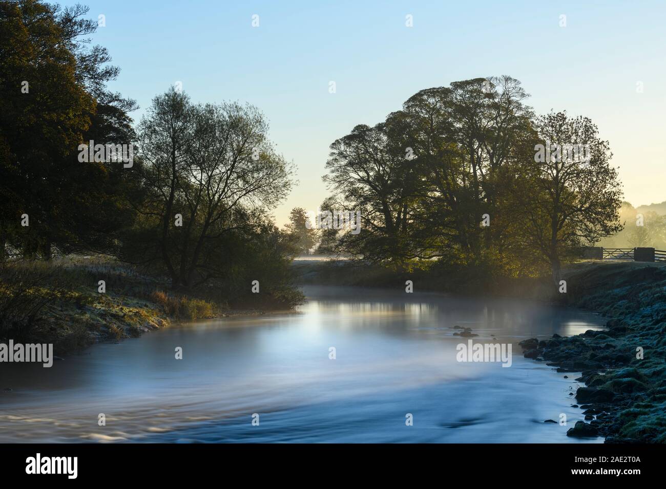 Cold early morning sunrise in scenic countryside, mist or fog lying over water of River Wharfe - Burley in Wharfedale, West Yorkshire, England, UK. Stock Photo
