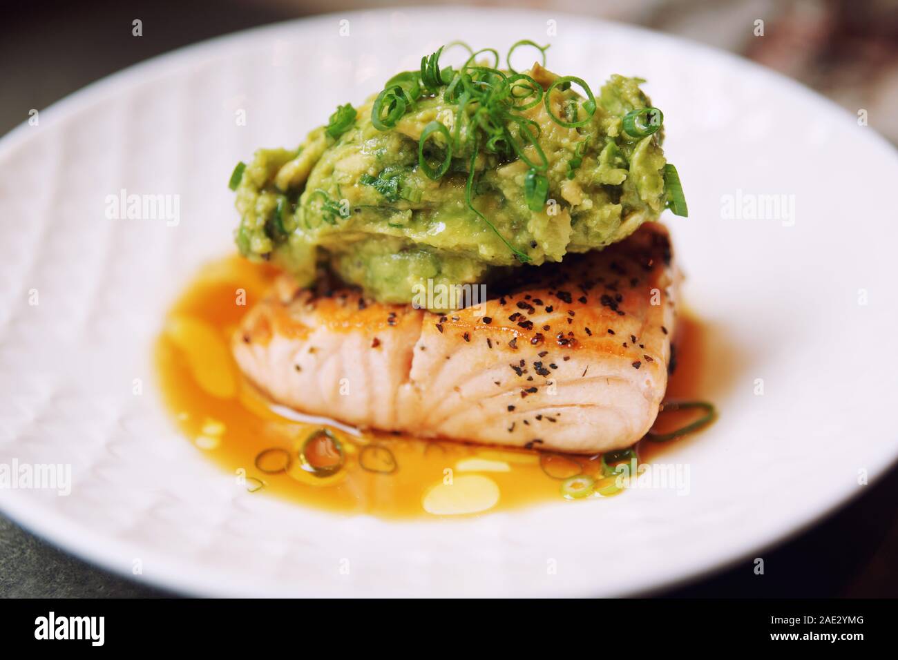 Grilled salmon fillet topped with avocado mash, leek and crushed nuts, cross-processing tone Stock Photo