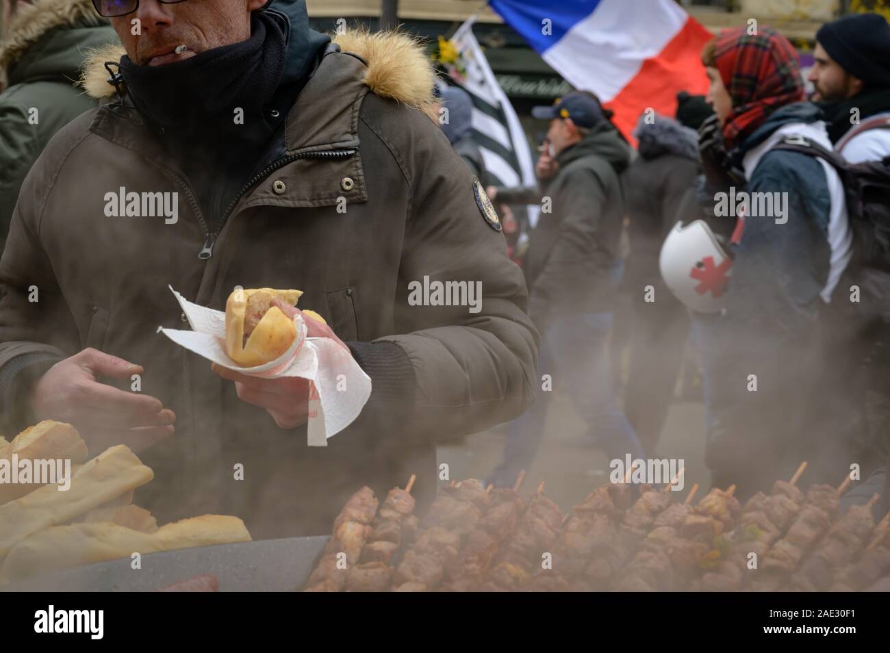 PARIS, FRANCE, DECEMBER 05 2019 : a protestor having some food at a street vendor during a 'Gilets Jaunes' (Yellow Vests) protest. Stock Photo