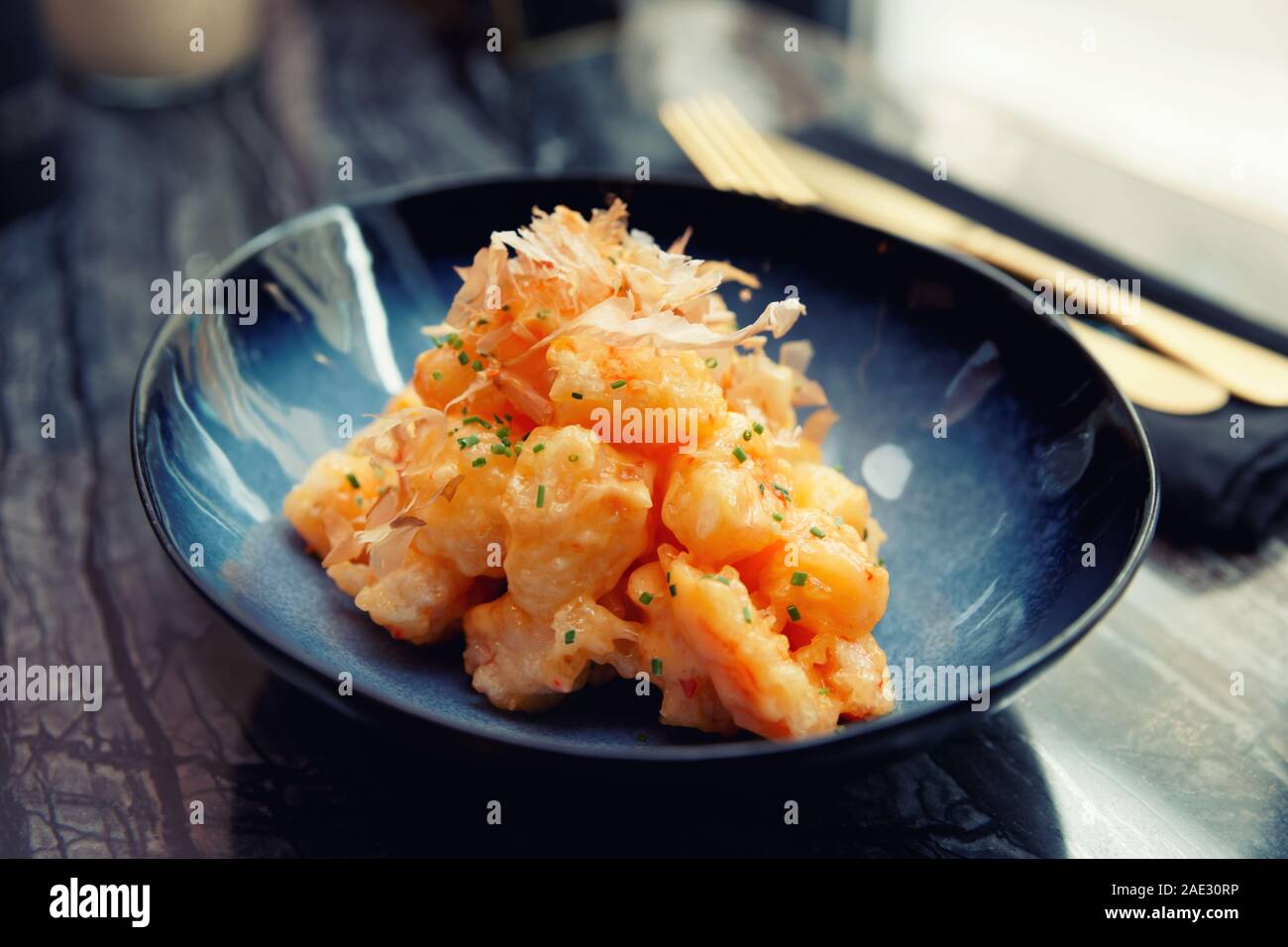 Shrimps cooked in Asian style in batter with sweet-sour sauce and bonito tuna on marble table, cross processing tone Stock Photo