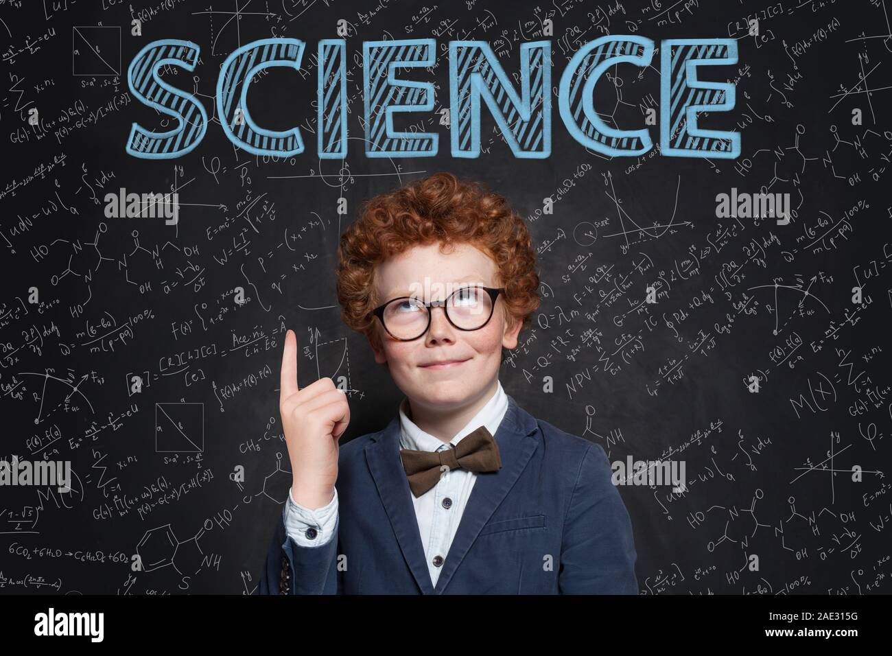 Smart confident kid boy with red hair pointing up at science inscription on chalkkboard Stock Photo