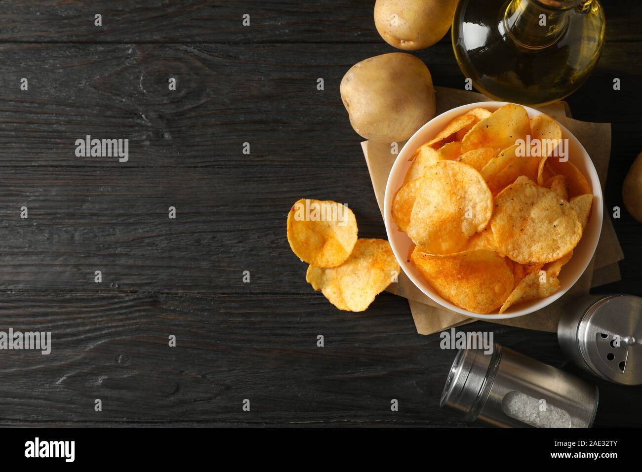 Potato chips in a bowl on craft paper. Potato, spice, olive oil on wooden background, space for text Stock Photo