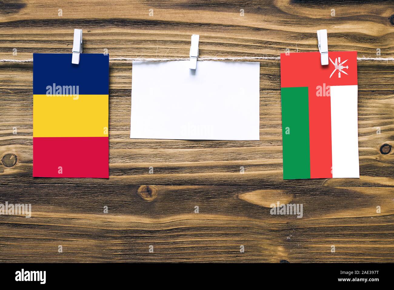 Hanging flags of Chad and Oman attached to rope with clothes pins with copy space on white note paper on wooden background.Diplomatic relations betwee Stock Photo