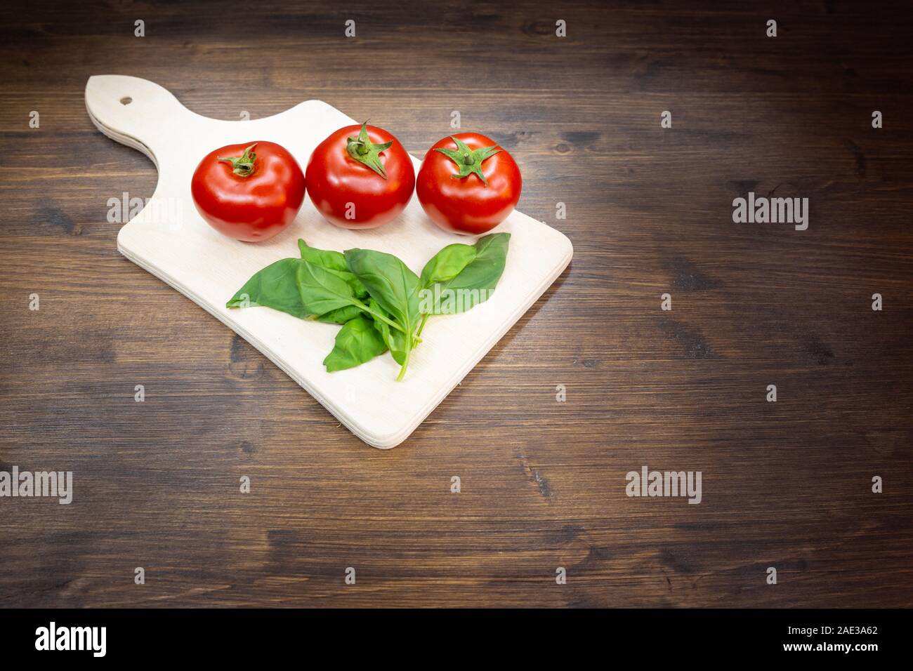 Tomatoes and basil arranged on a cutting board on an old table. Two ...