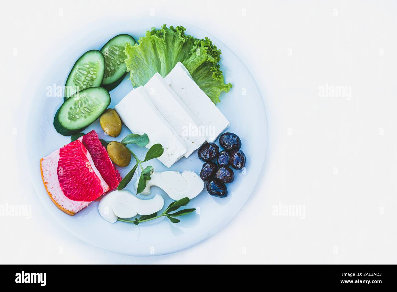 Feta cheese and sulguni on white plate with fresh vegetables and culinary plants on white background, closeup and copy space. Light, healthy breakfast Stock Photo