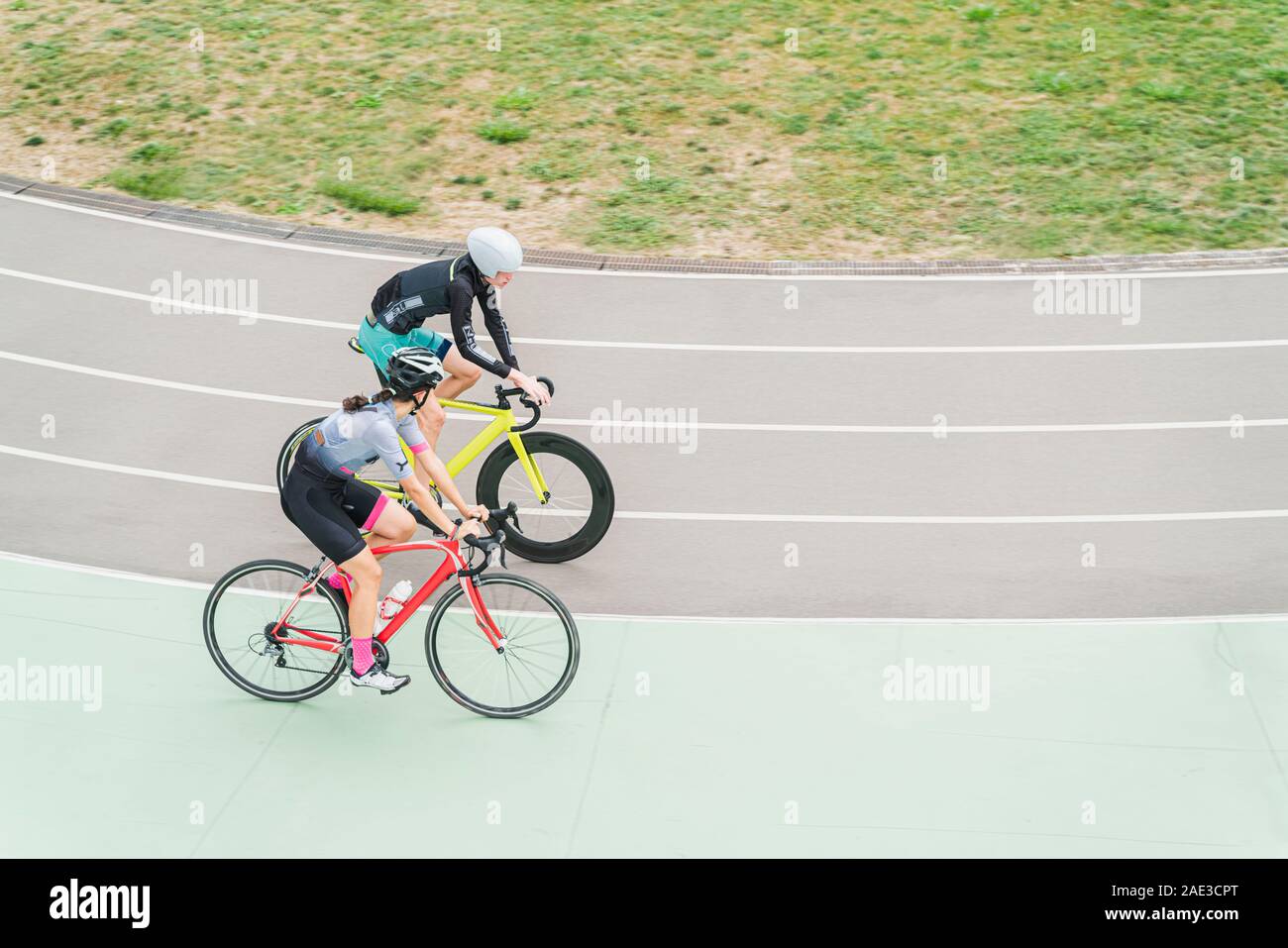 Young man and woman riding on bike track in athletic wear and helmet on the stadium. Two cyclers running bicycles together and enjoy this. Stock Photo