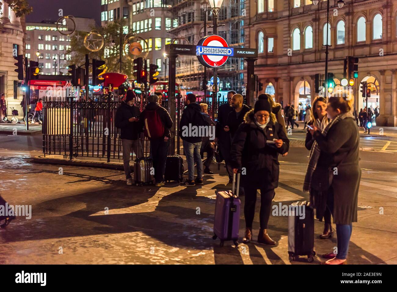 City of London at night. People gathered in Trafalgar Square outside entrance steps to Charing Cross underground station on a cold November evening. Stock Photo