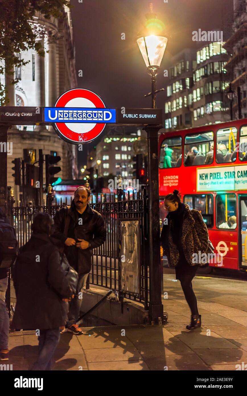 City of London lit up at night. People outside entrance to Charing Cross Underground Station, Trafalgar Square, central London UK. Double-decker bus. Stock Photo
