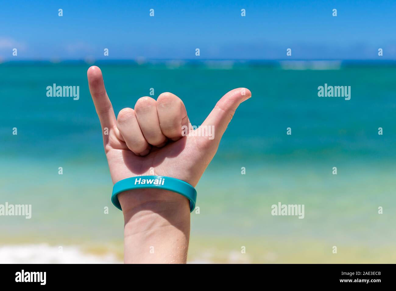 Hawaiian shaka sign. Hang Loose sign, being made with a blue sky and tropical sea in the background. Stock Photo