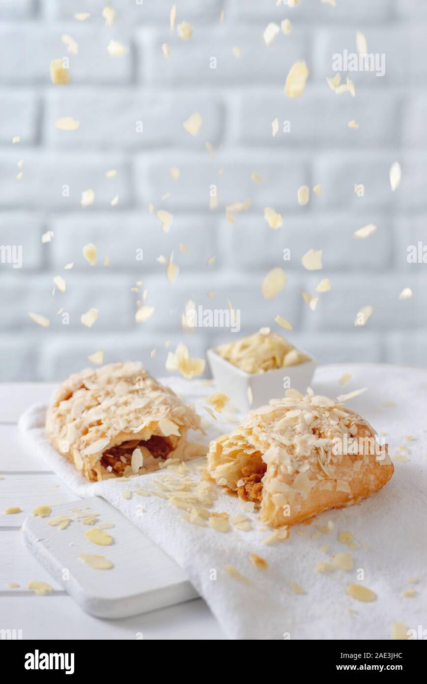 Almond flakes falling from above over caramel strudel on white brick background Stock Photo
