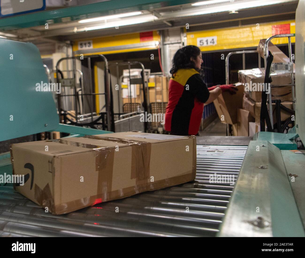 05 December 2019, Brandenburg, Börnicke: A DHL employee loads parcels from a tug onto a conveyor belt at the DHL-Paketzentrum. During Advent, up to 570,000 shipments a day arrive at their destination from Börnicke, with 200 additional employees deployed. Photo: Monika Skolimowska/dpa-Zentralbild/ZB Stock Photo