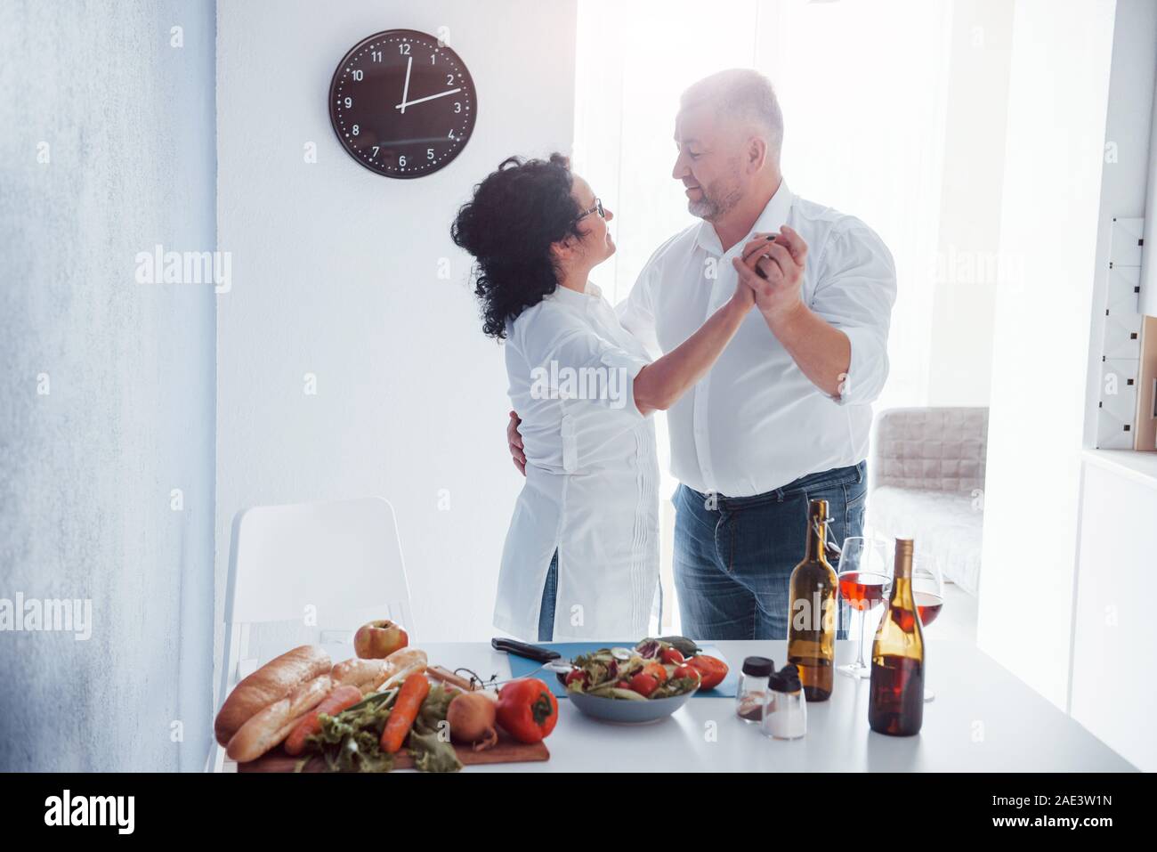 Romantic dinner. Senior man and his wife in white shirt on the kitchen Stock Photo