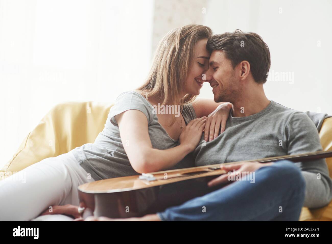 In love with each other. Guitar on the legs. Happy couple relaxing on the yellow sofa in the living room of their new house Stock Photo