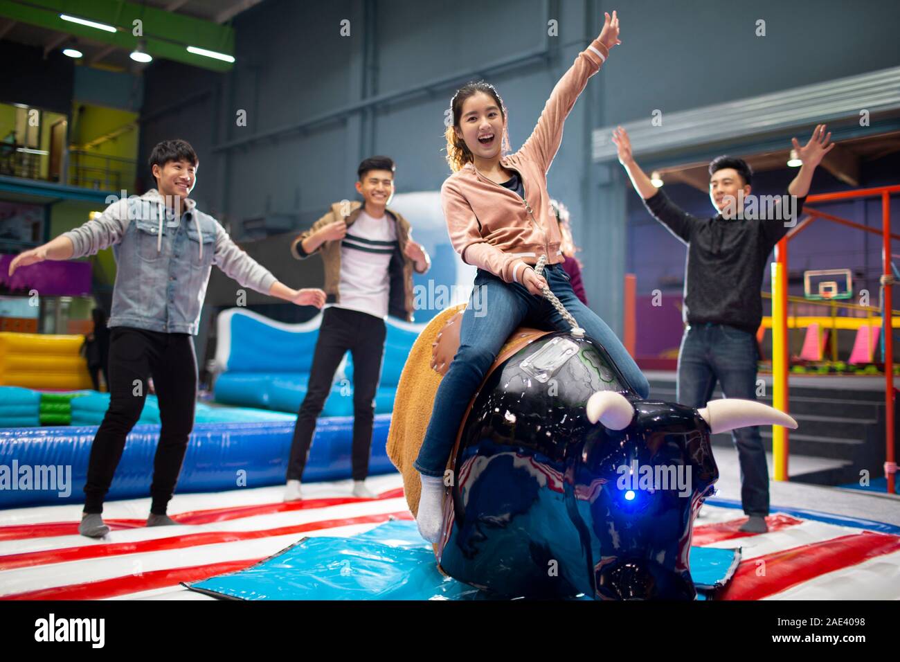 Happy young friends playing mechanical bull game Stock Photo