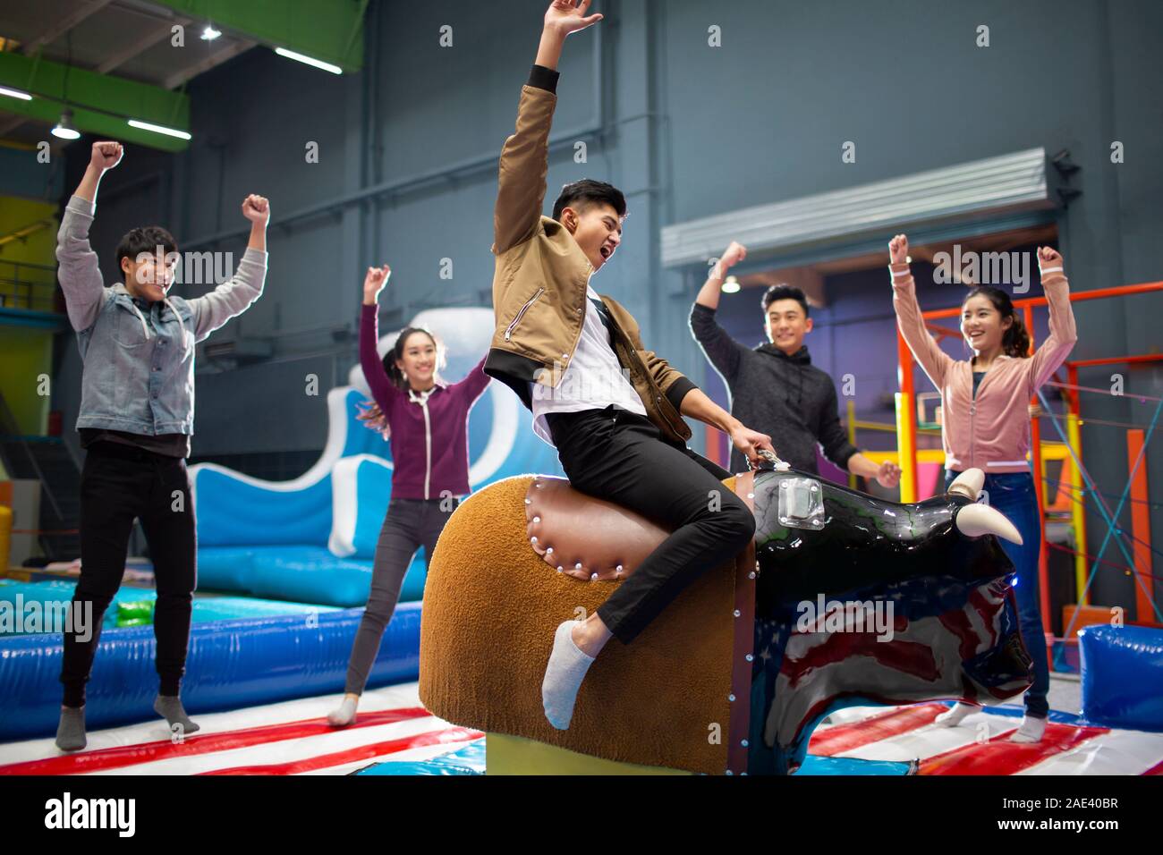 Happy young friends playing mechanical bull game Stock Photo