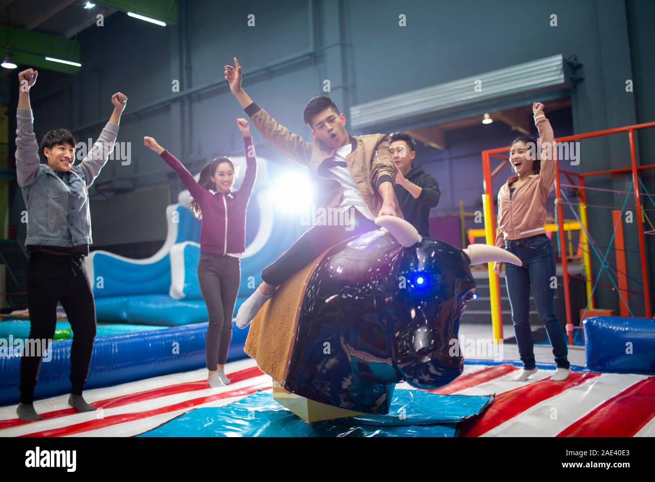 Happy young friends playing mechanical bull game Stock Photo
