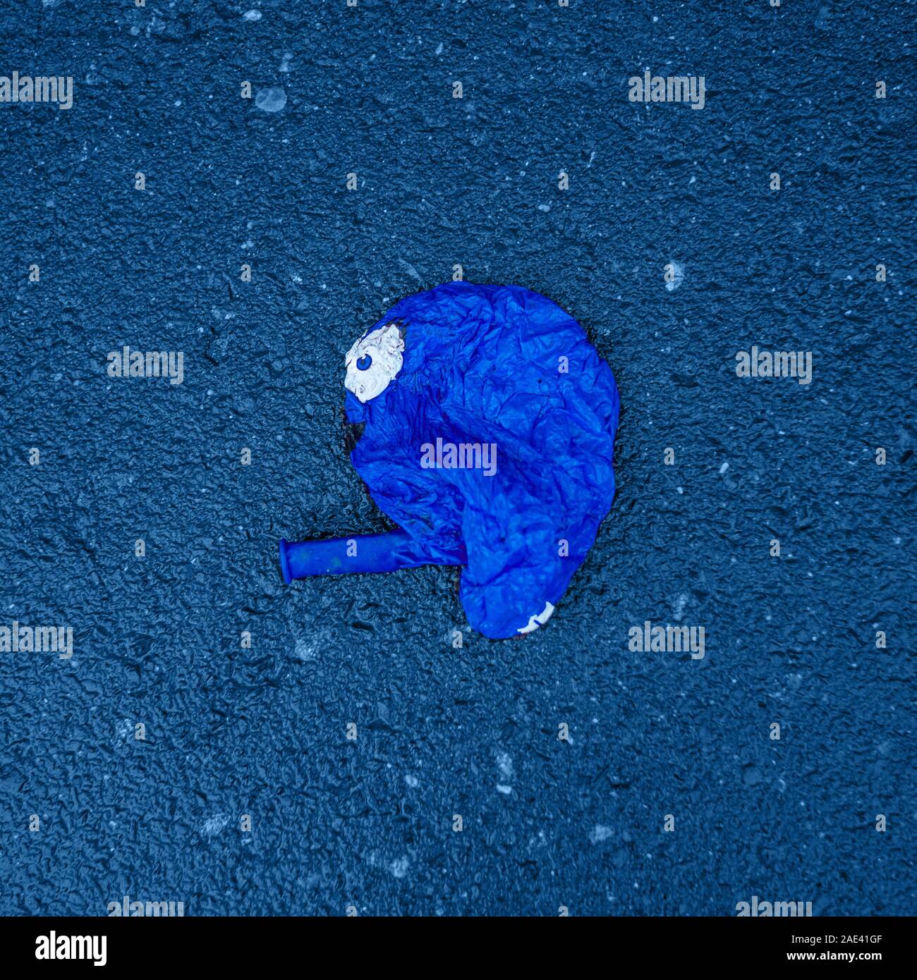 A puffed up blue air balloon with a funny face lies on the pavement. Stock Photo