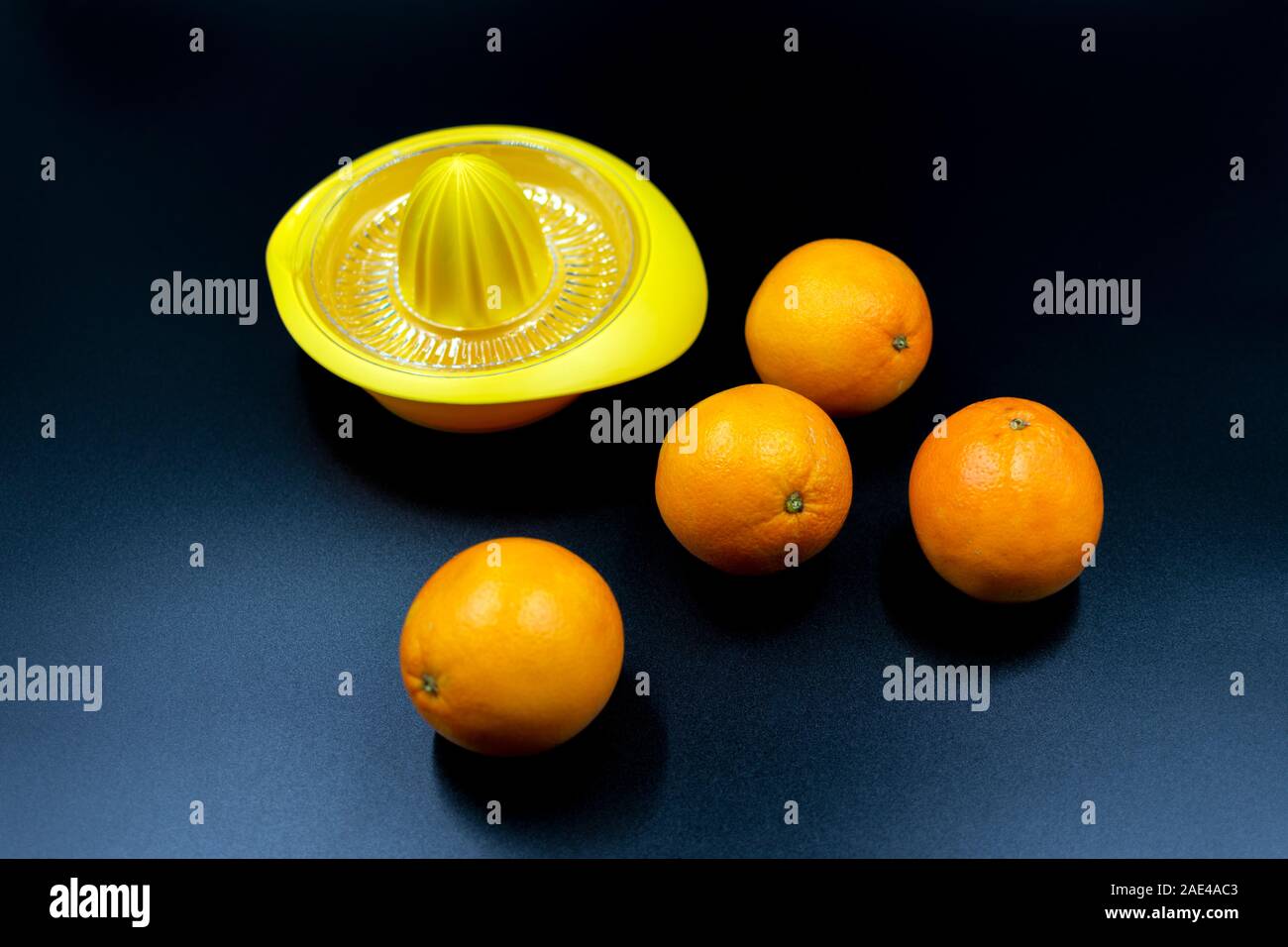 yellow orange squeezer with oranges on dark blue background Stock Photo -
