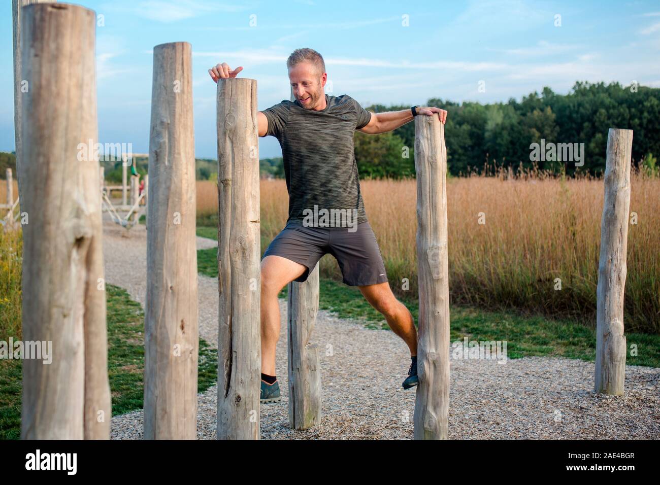 A happy man walks across a series of wooden poles on obstacle course Stock Photo