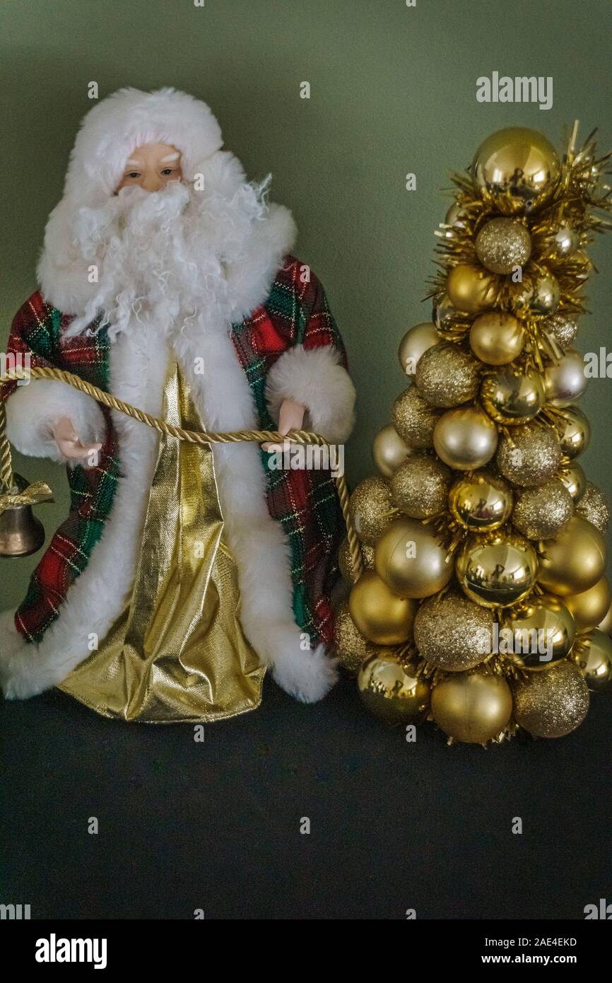 A Santa Claus figurine holding a rope attached to a bell and a bunch of gold color globes Stock Photo