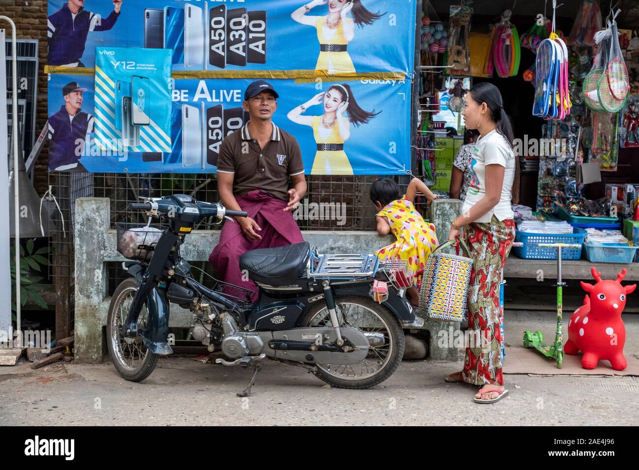 A young Burmese mother with her daughter negotiates a fare with a motorbike driver to take her home after shopping in Homalin, Myanmar (Burma) Stock Photo
