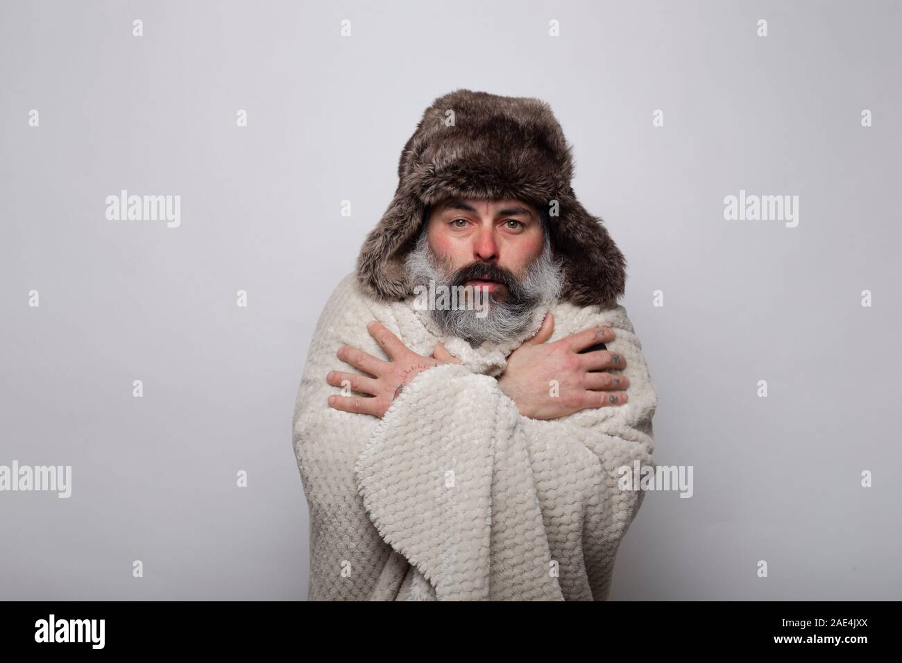 mature man covering himself with a blanket and with a hat shaking in the cold.M Stock Photo