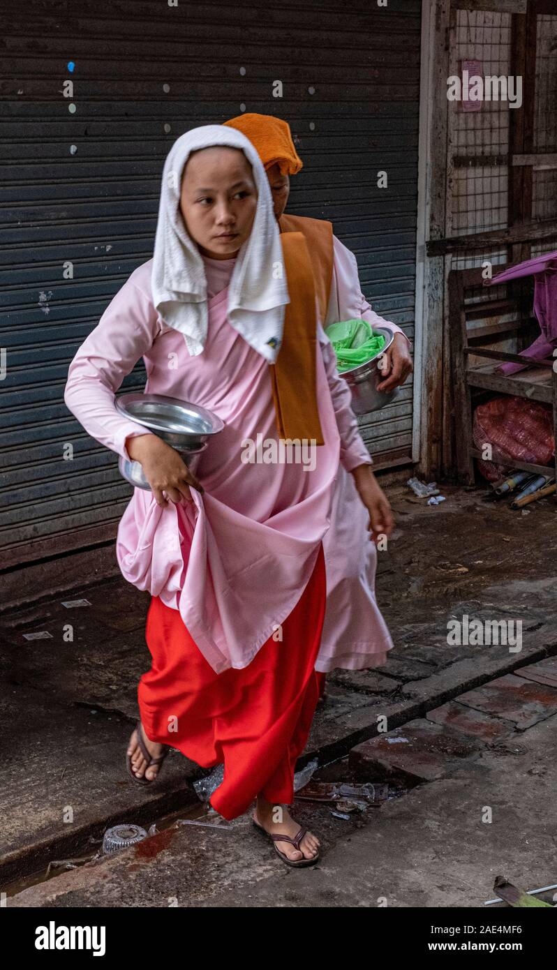 Buddhist nuns pass through a market with their alms bowls in search of donations during a holy day in Mandalay, Myanmar (Burma) Stock Photo