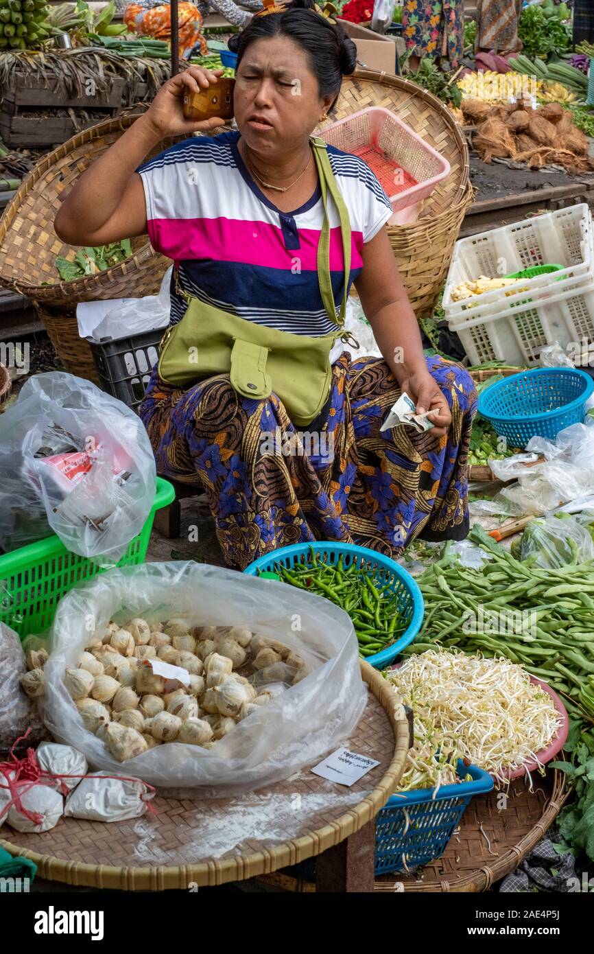 A Burmese woman on a mobile phone sells fresh vegetables and betel nut in the railroad market of Mandalay, Myanmar (Burma) Stock Photo